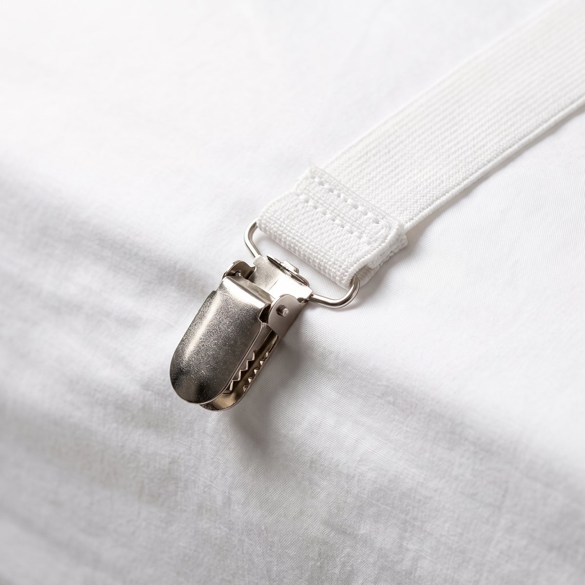 Close-up of a Bedly Strap clip fastened to a white fitted sheet on a dorm bed