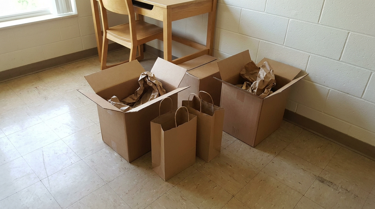 Plain cardboard boxes and unmarked paper shopping bags on the floor of an empty dorm room on move-in day